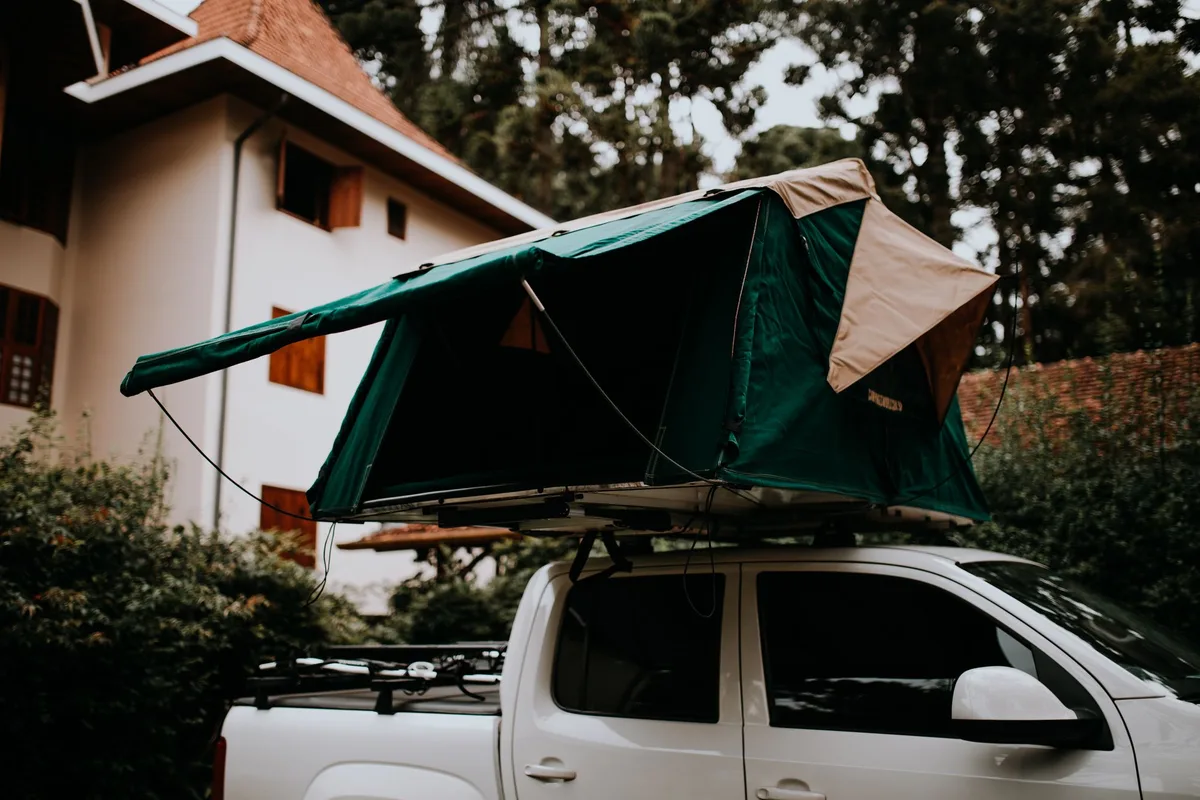 An open green rooftop tent on a white pickup beside a house